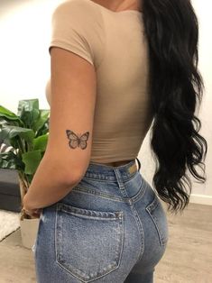 a woman with a butterfly tattoo on her left arm and right leg, standing in front of a plant