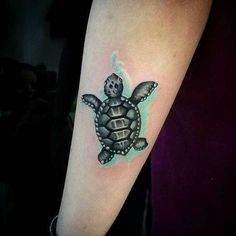 a small turtle tattoo on the right forearm and arm, with an aqua glow behind it