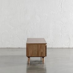 a small wooden table sitting on top of a cement floor next to a white wall