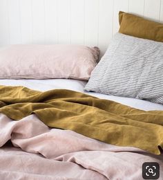 an unmade bed with pink and yellow sheets on it, along with two pillows