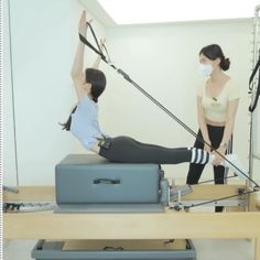 a woman in a white shirt is doing pivots on an exercise machine while another woman watches