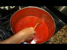 a person stirring red sauce in a pot on the stove with a wooden spatula