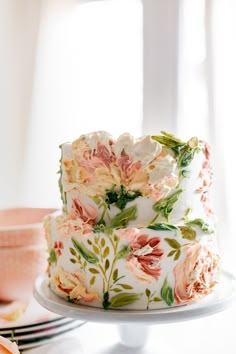 a white cake with pink and green flowers on it sitting on top of a table