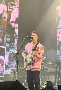 a man standing in front of a microphone on top of a stage holding a guitar