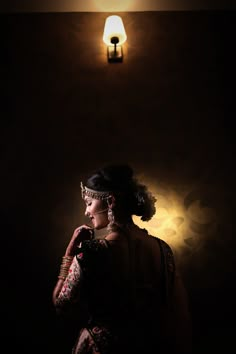 a woman standing in front of a wall light with her hands on her face and looking off to the side