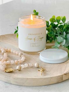 a candle and rosary on a wooden tray next to some greenery in the background