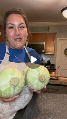 a woman holding two heads of cabbage in her hands while standing next to a kitchen counter