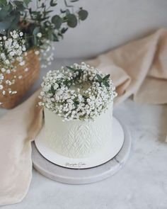 a white wedding cake with baby's breath flowers on top, sitting next to a potted plant