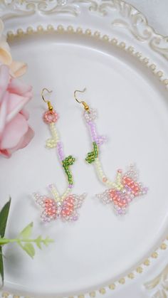 two pairs of earrings sitting on top of a white plate next to a pink flower