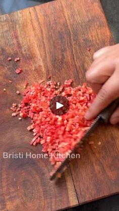 a person cutting up red food on top of a wooden table with a large knife