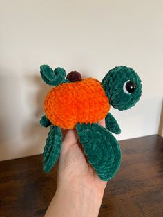 a hand holding an orange and green stuffed animal