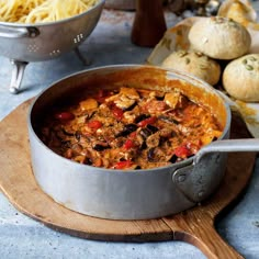 a pot full of food sitting on top of a wooden cutting board next to some bread