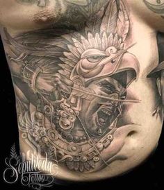 a man's chest with an eagle and helmet tattoo on his stomach, which is surrounded by other tattoos