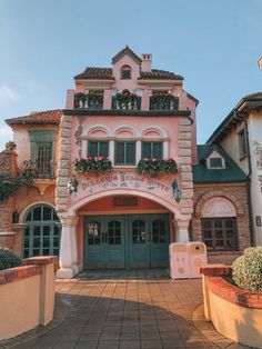 a pink and green building with flowers on the balcony above it's entrance door