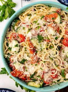 a blue bowl filled with pasta, tomatoes and parmesan cheese covered in herbs