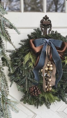 a wreath hanging on the front door with pine cones, bells and blue satin bow