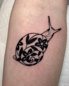 a black and white snail tattoo on the right leg, with flowers in it's shell