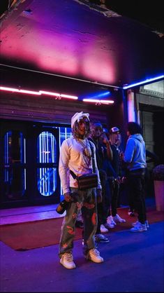 a group of people standing around in front of a building with purple lights on it