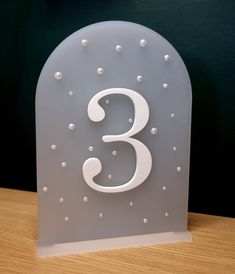 the number three is made out of frosted glass and sits on a wooden table