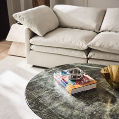 a coffee table with a book on it in front of a white couch and pillows