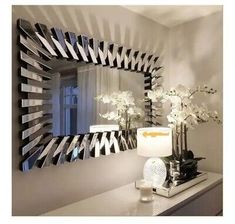 a mirror sitting on top of a dresser next to a lamp and vase with flowers