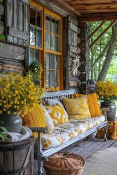 a porch with yellow and white pillows on it, flowers in vases next to the couch