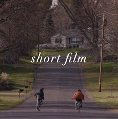 two bicyclists riding down the road in front of a house with short film written on it