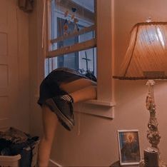 a woman bending over in front of a window next to a lamp and pictures on the wall