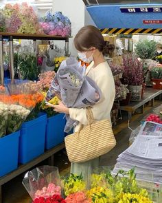 a woman wearing a face mask and holding flowers in a flower shop with blue bins