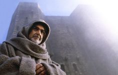 an old man wearing a coat and scarf standing in front of a castle