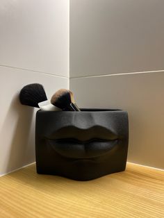 there is a black container with two makeup brushes in it on the floor next to a white wall