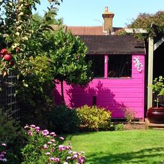 a pink shed is next to some flowers and trees