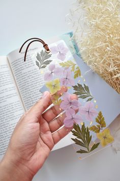 a hand holding an open book with flowers on it and a string attached to the cover