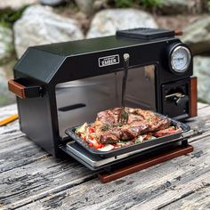 a grill that has some food in it on top of a wooden table next to rocks