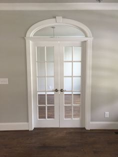 an empty room with two white doors and wood floors in the center is seen from across the room