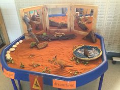 an orange sand play area with toys and animals in the center, including a blue table