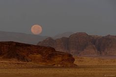 the moon is setting in the sky over some mountains and desert land with no people on it