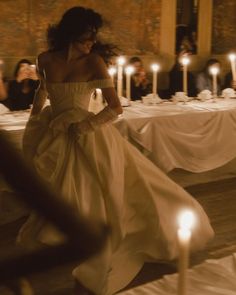 a woman in a white dress is walking through a room with candles on the tables