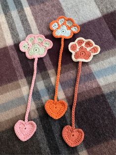 three crocheted flowers and hearts on a plaid blanket, one is orange the other is pink