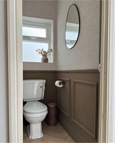 a white toilet sitting next to a window in a bathroom under a large round mirror