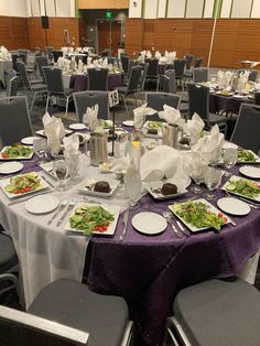 a banquet hall with tables and chairs covered in purple table cloths, place settings and silverware