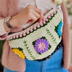 a woman is holding a crocheted purse with flowers on the front and sides