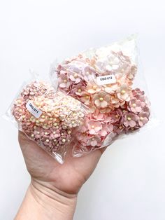 a hand holding two bags filled with pink and white flowers on top of each other