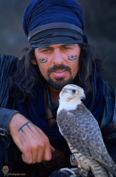 a man with tattoos on his face and an owl perched on his arm in front of him