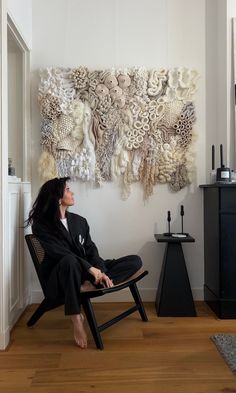 a woman sitting on a chair in front of a wall hanging with intricate paper art