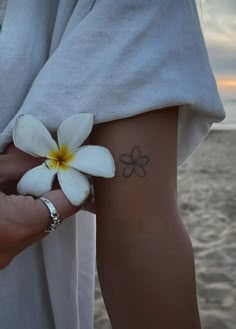 a woman with a flower tattoo on her left arm next to the ocean at sunset