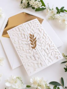 a white card with a gold leaf on it next to some flowers and greenery