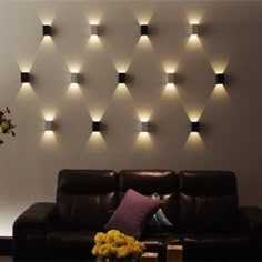 a living room with couches and lights on the wall above it, along with a vase filled with yellow flowers