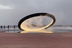 a group of people standing in front of a body of water with a large circular object on it's side