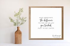 there is a vase with some flowers in it next to a framed quote on the wall